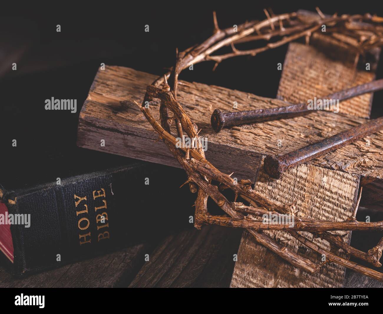 Primo piano di croce di legno e corona di spine con la Bibbia Santa in un ambiente rustico scuro Foto Stock