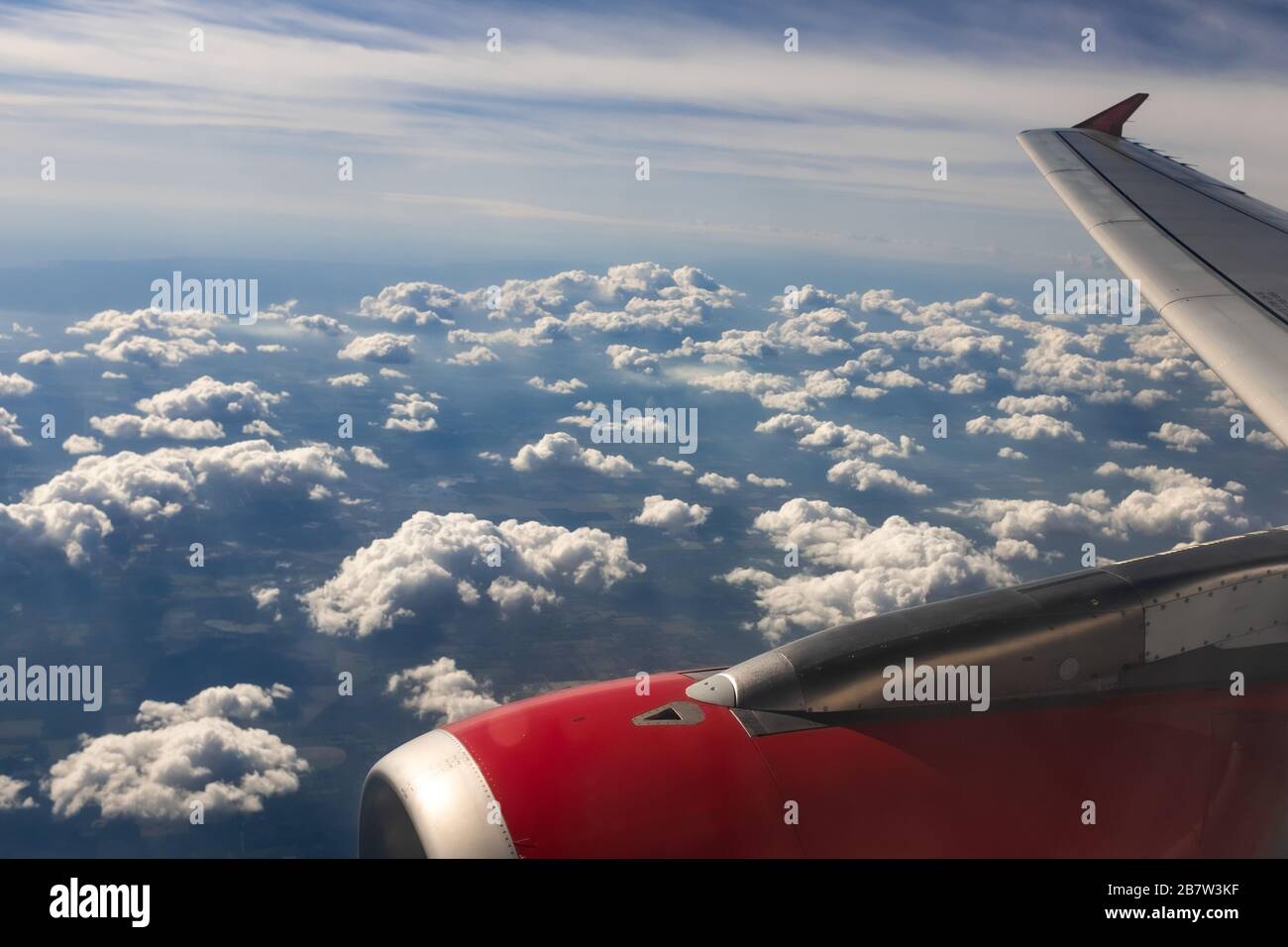 Un'immagine del paesaggio a colori che si affaccia attraverso la finestra dell'aeroplano e mostra terra, nuvola e cielo. Foto Stock