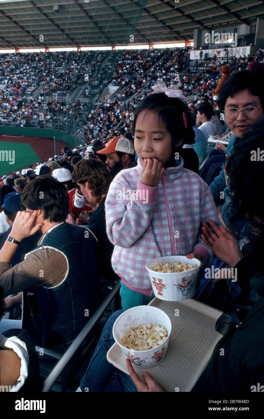 Austin Texas USA: Snack ragazza asiatica-americana mentre frequenta la partita di baseball dell'università con la sua famiglia. SIGNOR ©Bob Daemmrich Foto Stock