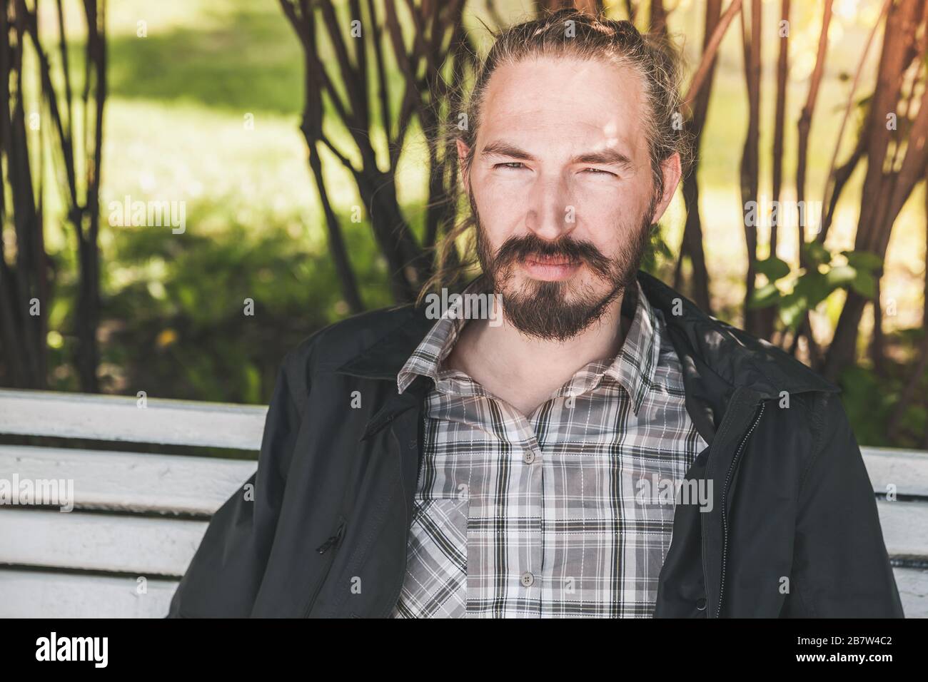 Giovane uomo asiatico barbuto seduto su una panchina nel parco estivo, ritratto all'aperto Foto Stock