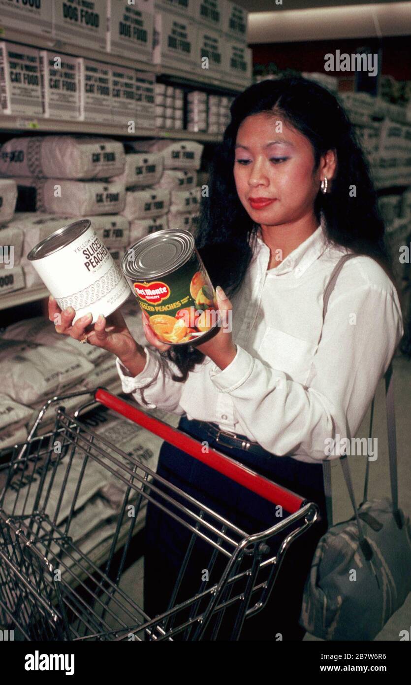 Austin Texas USA: Donna asiatica-americana che confronta pesche generiche e di marca in scatola al negozio di alimentari. SIGNOR ©Bob Daemmrich Foto Stock
