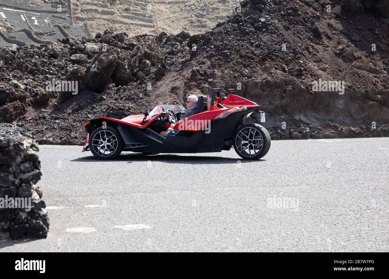 Il kit auto rosso a tre ruote si muove tra la roccia vulcanica fusa di lava a Lanzarote, nelle Isole Canarie Foto Stock