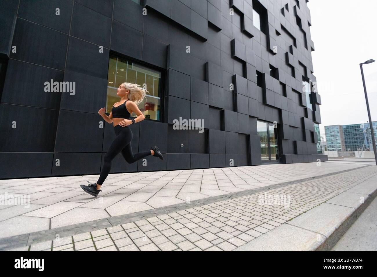 Donna in corsa veloce che indossa il top sportivo in un ambiente urbano moderno Foto Stock