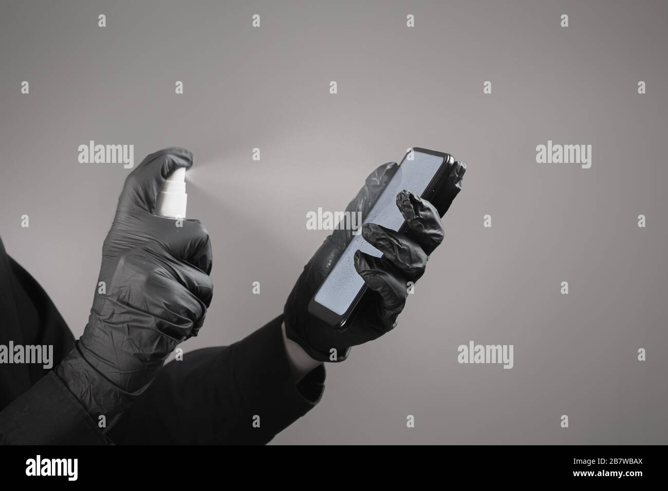 Pulizia del telefono con un igienizzatore, concetto di nero totale. Mani in guanti neri spray disinfettante sullo schermo dello smartphone. Prevenzione diffusione virus conc Foto Stock