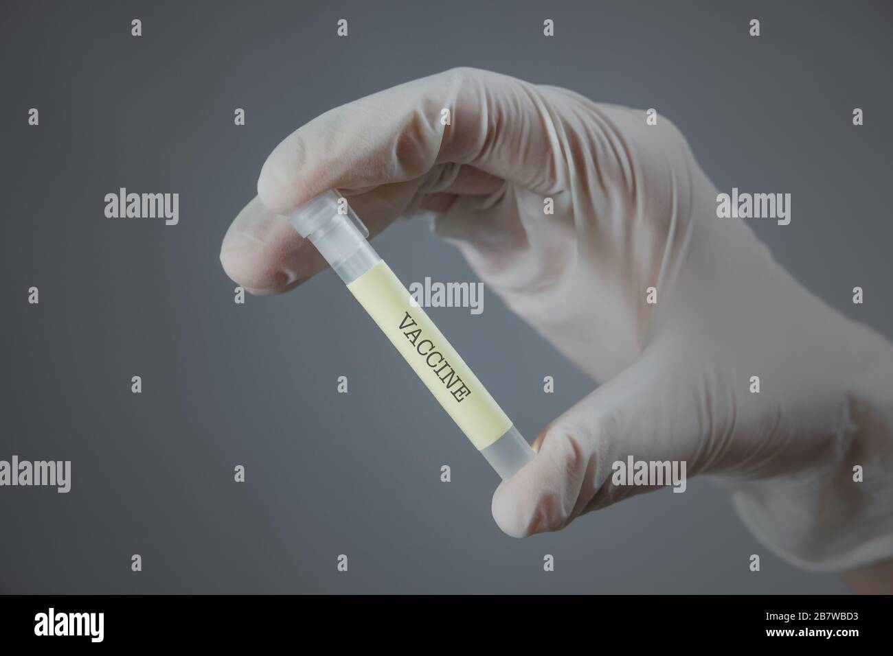 Mano in guanto medico con un contenitore da laboratorio - segno 'vaccino' su di esso. Vaccinazione, ricerca virale o concetto di sviluppo del trattamento Foto Stock