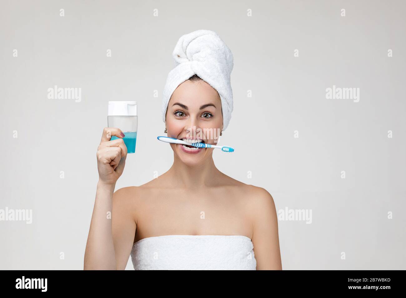 Giovane donna felice in asciugamano spazzolare i denti al mattino. Ragazza che tiene spazzolino e collutorio gel per sciacquare bocca, respiro fresco. Denti e denti concetto di salute. Foto Stock