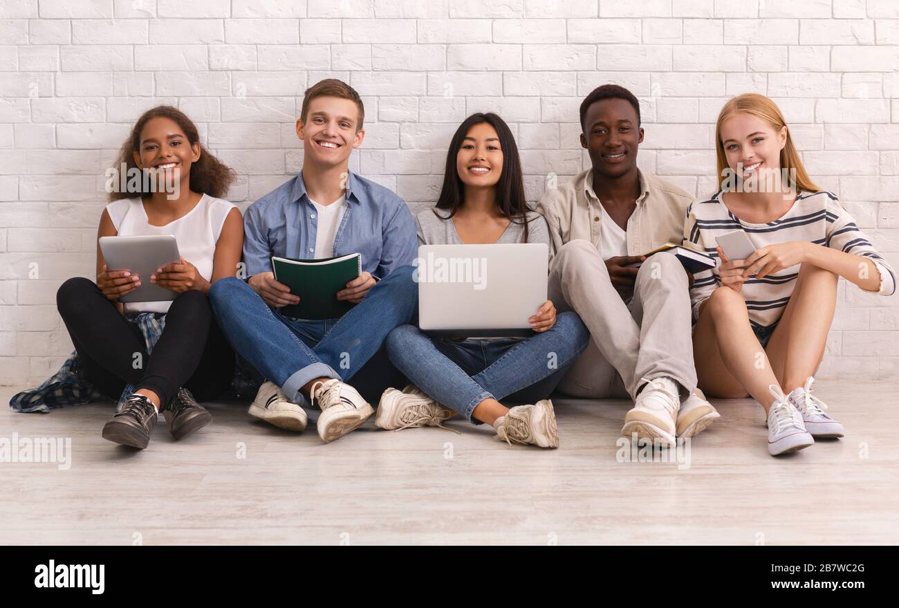 Gruppo sorridente di studenti internazionali che studiano su un muro di mattoni bianchi Foto Stock