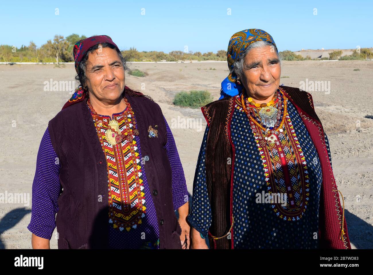 Due donne in posa che indossano abiti tradizionali per l'area rurale in Asia Centrale a Kunya Urgench, Turkmenistan. Colorful Turkmen accappatoio e sciarpa. Foto Stock