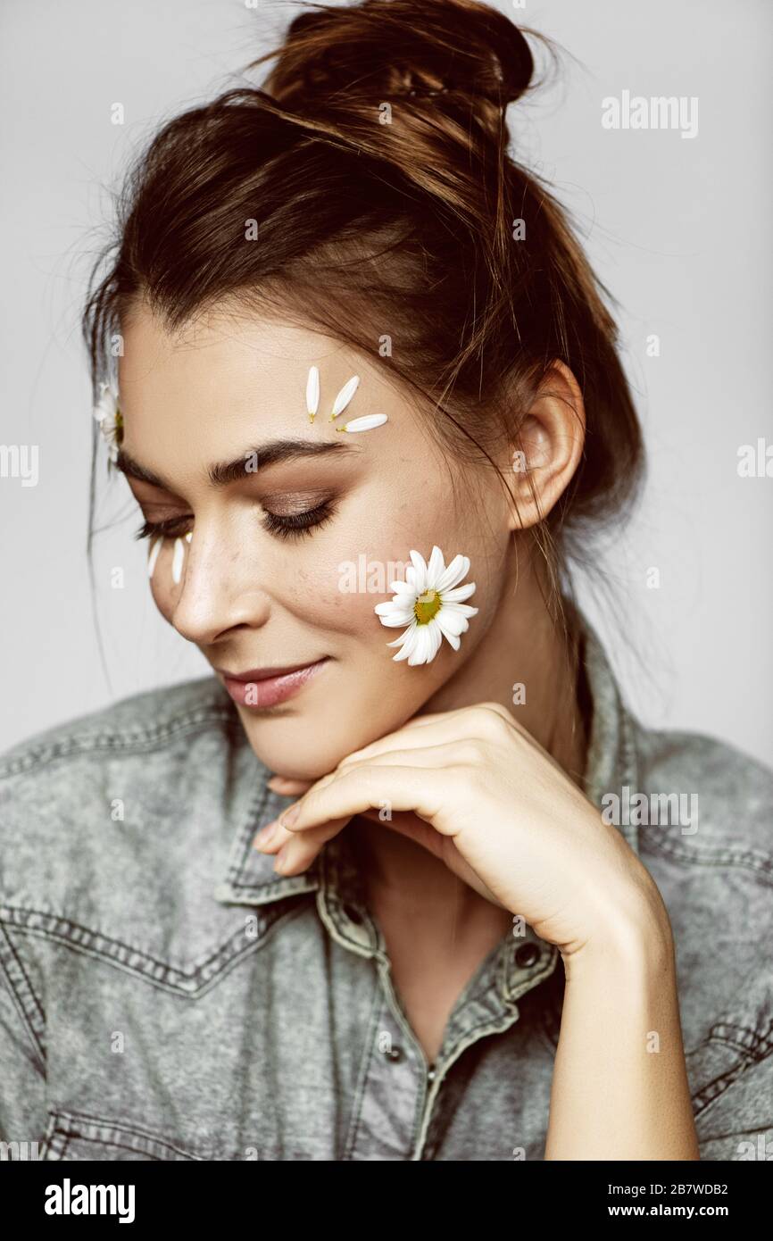 Bella giovane donna con fiori sul viso e mano sul mento guardando verso il basso. Concetto di primavera. Foto Stock