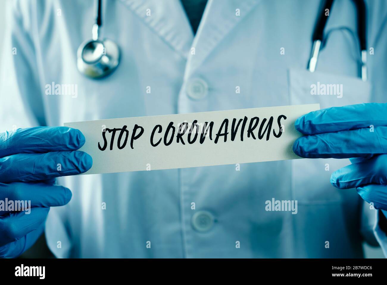 primo piano di un medico, indossando guanti chirurgici blu, mostrando il messaggio stop coronavirus scritto in un pezzo di carta Foto Stock