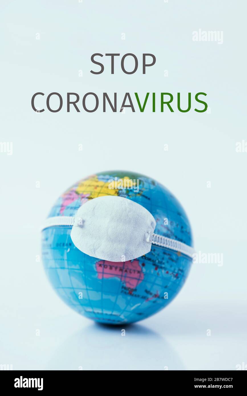 primo piano di un globo terrestre con una maschera protettiva e il testo fermare il coronavirus su uno sfondo bianco Foto Stock