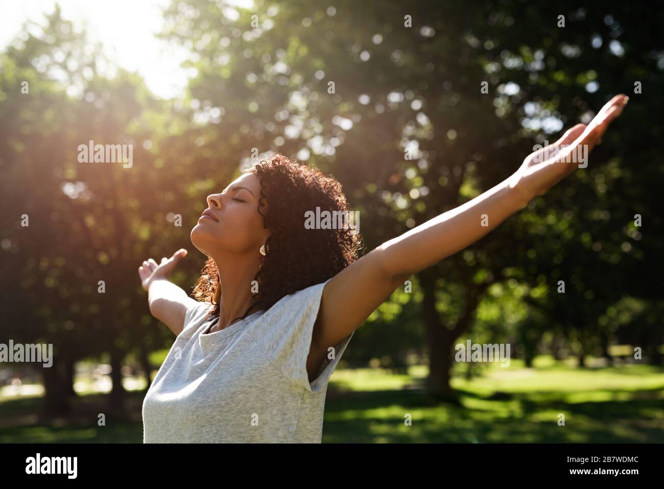 Donna in piedi in un parco che si rastrella le braccia verso l'alto Foto Stock