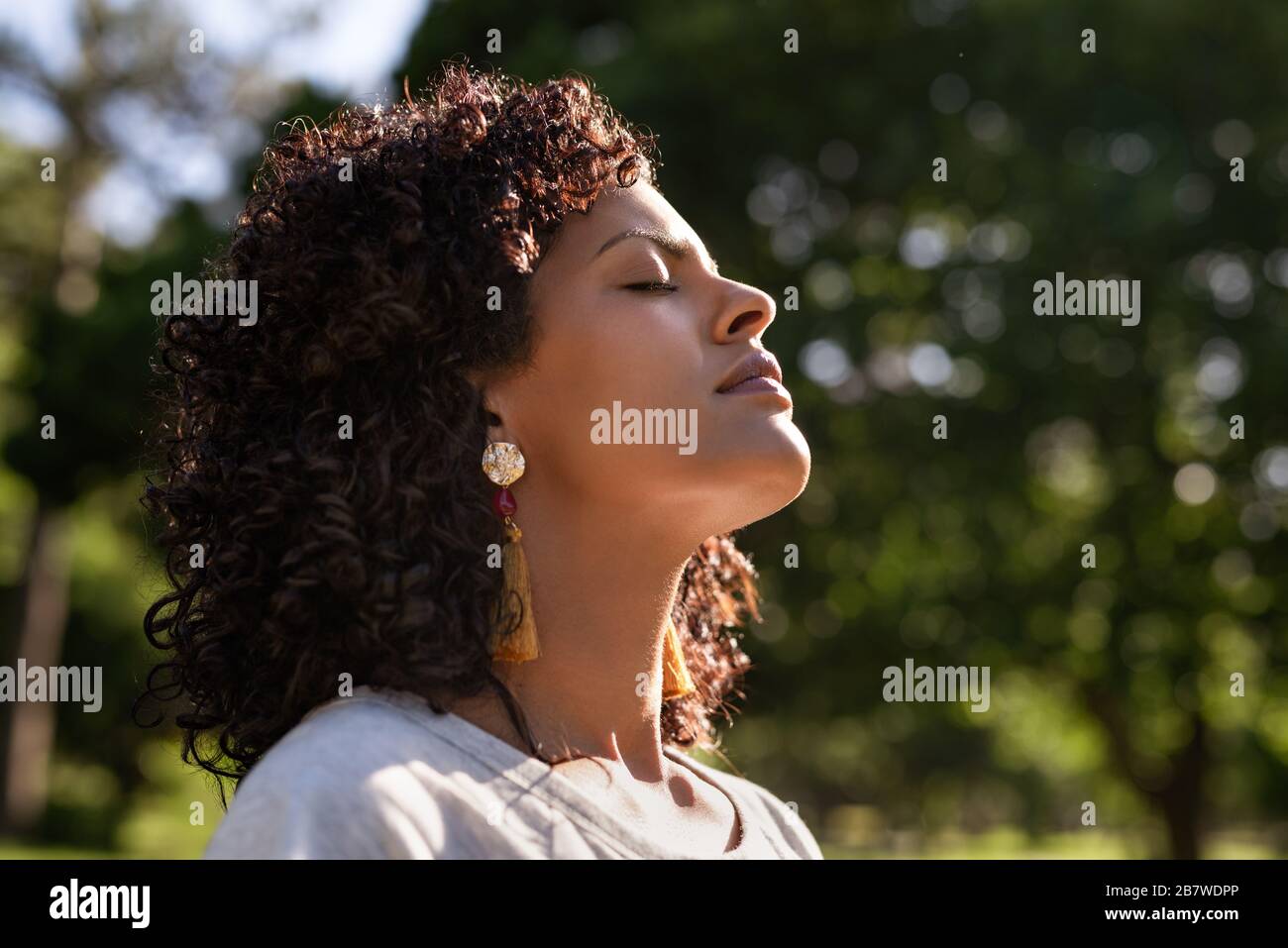 Giovane donna in piedi fuori sentire il sole sulla sua faccia Foto Stock