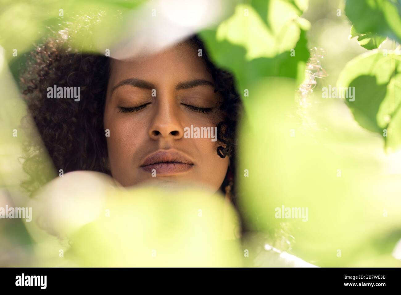 Giovane donna con gli occhi chiusi incorniciato da foglie verdi Foto Stock