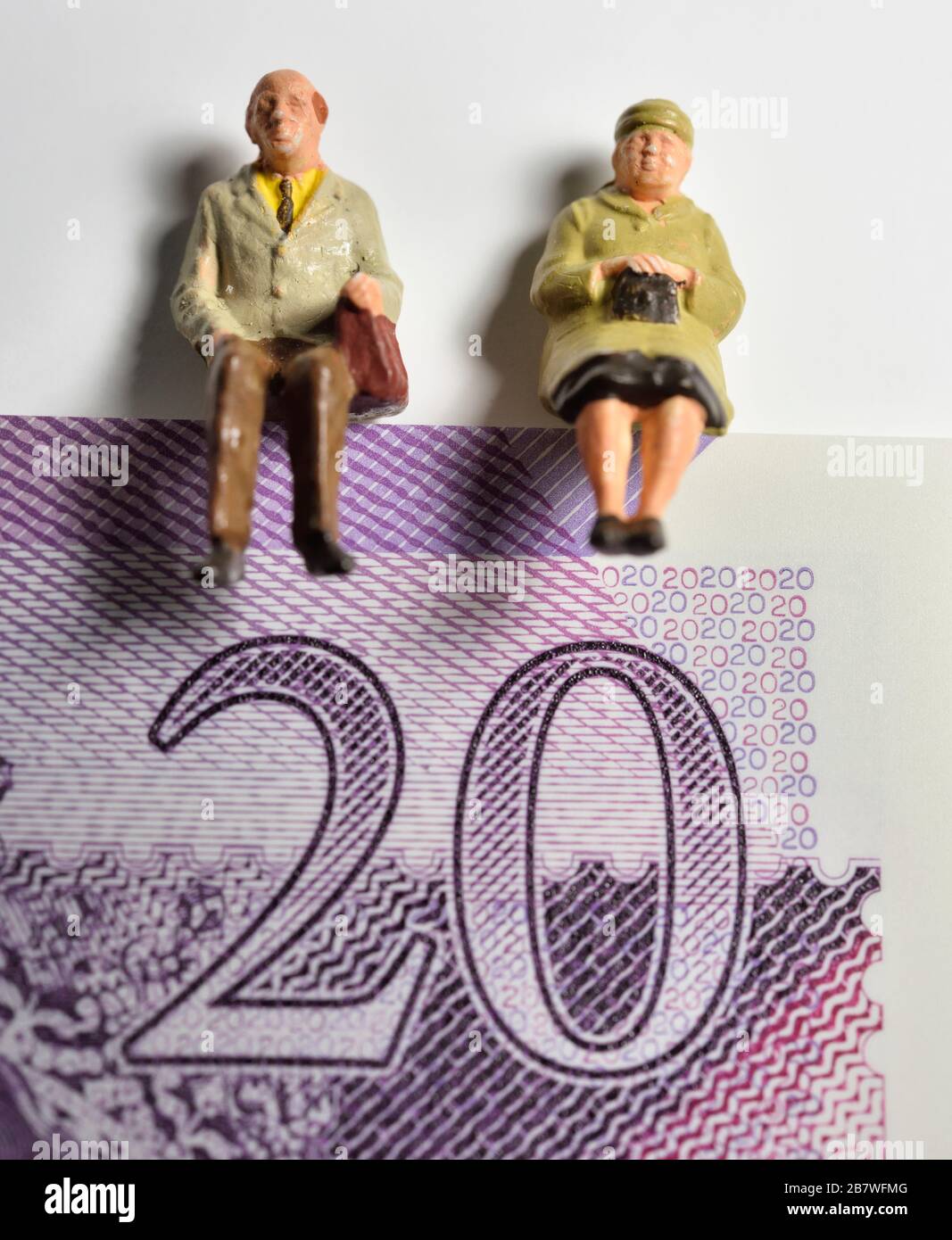 Figurina in miniatura pensionato coppia seduta in cima a una nota di venti libbre, concetto di pensione, concetti Foto Stock