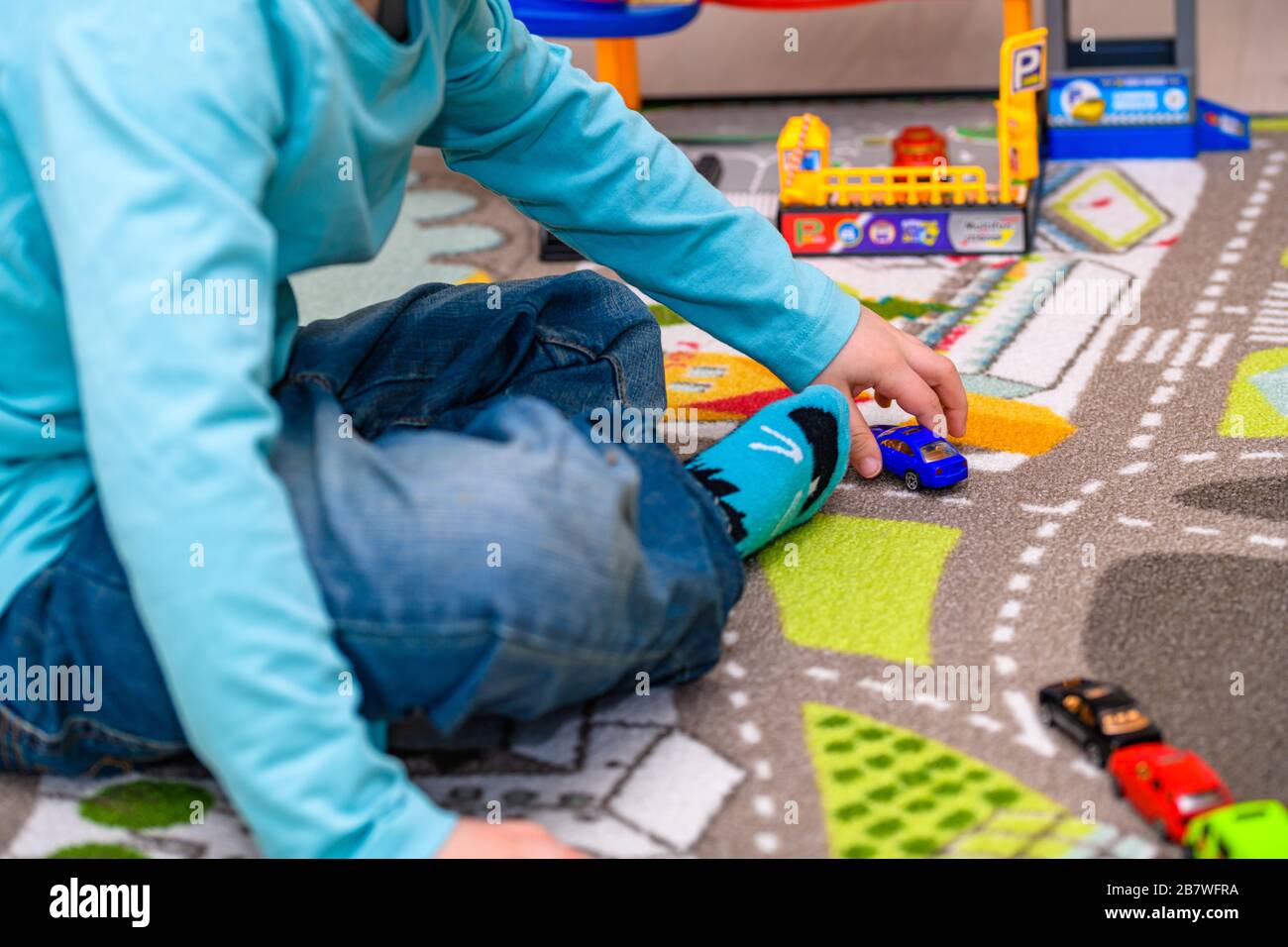 Ragazzo di cinque anni che gioca e allineano le auto giocattolo su un tappetino da gioco con le strade. Il ragazzo è vestito con jeans blu e una camicia turchese. Foto Stock