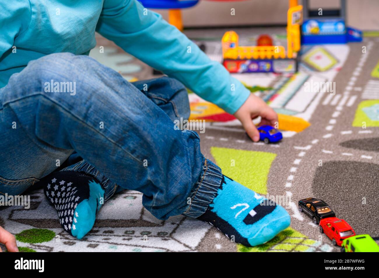Ragazzo di cinque anni che gioca e allineano le auto giocattolo su un tappetino da gioco con le strade. Il ragazzo è vestito con jeans blu e una camicia turchese. Foto Stock