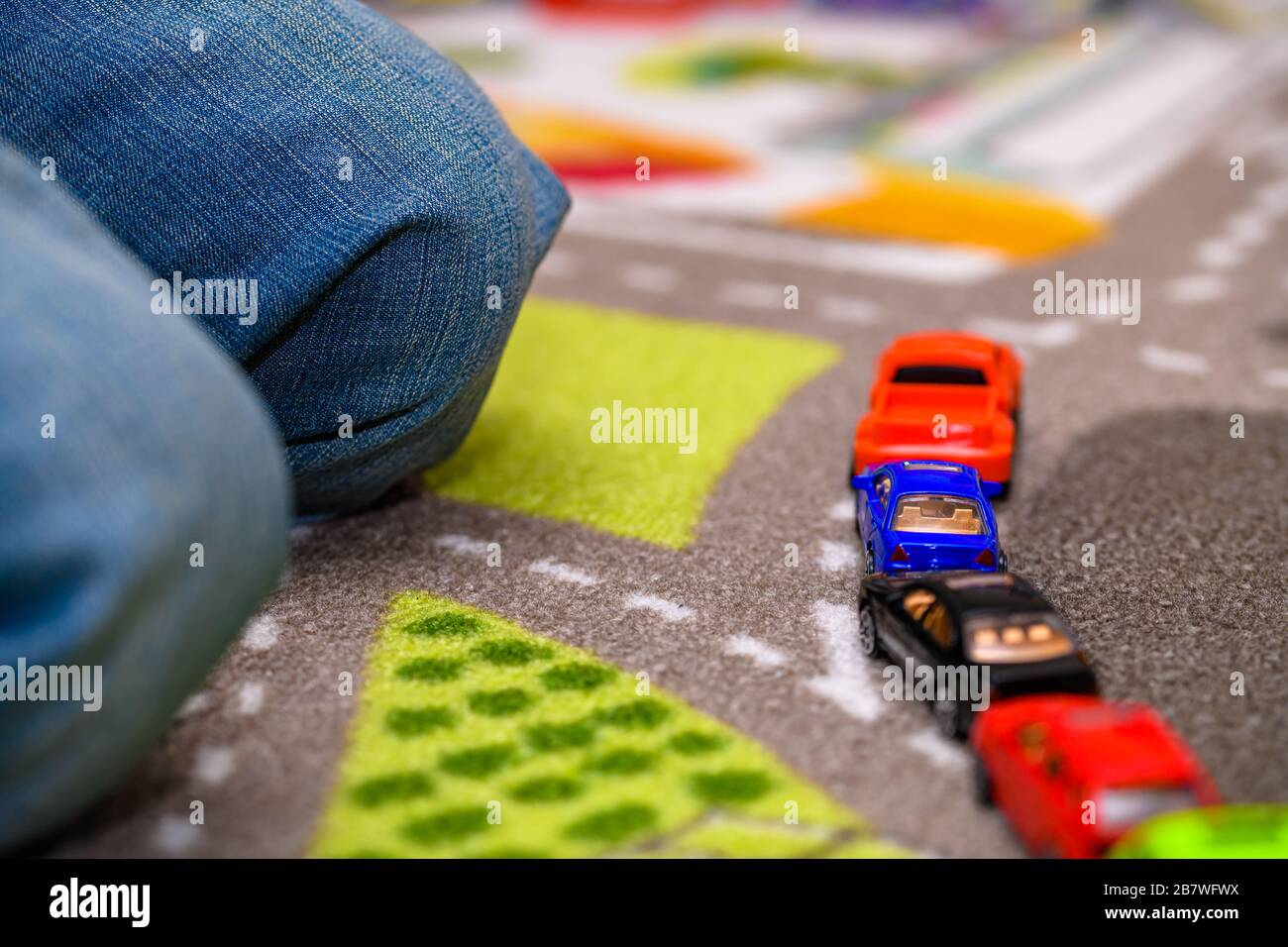 Primo piano di un ragazzo di cinque anni che gioca e allineano le auto giocattolo su un tappetino da gioco con le strade. Le vetture hanno colori vivaci. Foto Stock