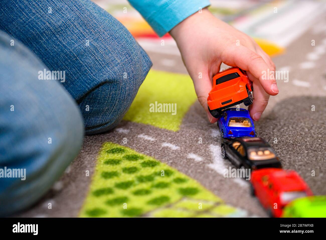 Primo piano di un ragazzo di cinque anni che gioca e allineano le auto giocattolo su un tappetino da gioco con le strade. Il ragazzo è vestito di jeans blu e tiene una macchina rossa. Foto Stock