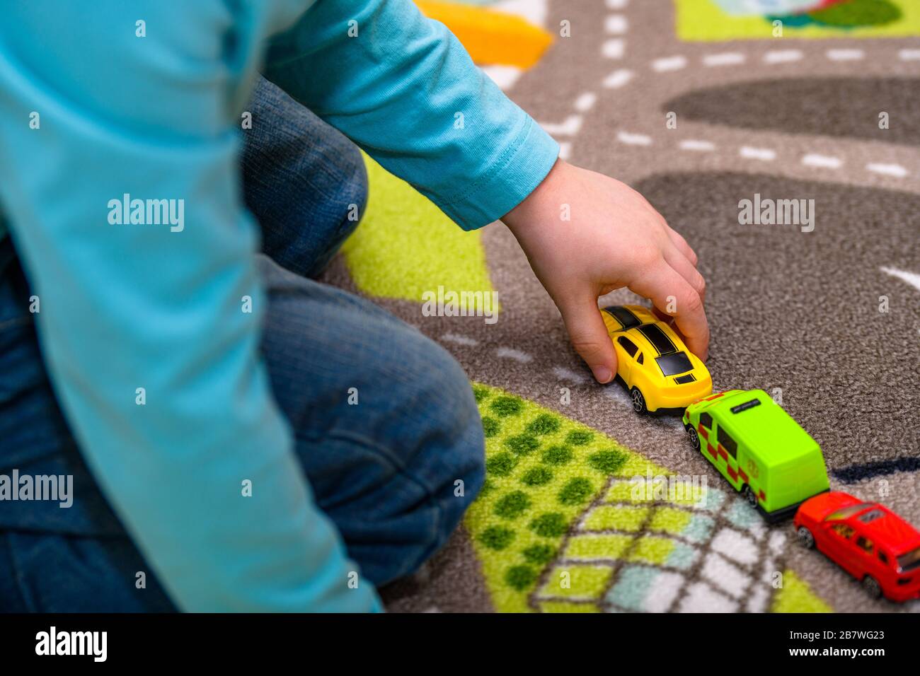 Primo piano di un ragazzo di cinque anni che gioca e allineano le auto giocattolo su un tappetino da gioco con le strade. Il ragazzo è vestito di jeans e tiene una macchina giocattolo gialla. Foto Stock