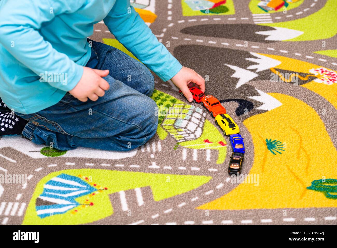 Ragazzo di cinque anni che gioca e allineano le auto giocattolo su un tappetino da gioco con le strade. Il ragazzo è vestito di jeans blu e di un giocattolo rosso in mano. Foto Stock