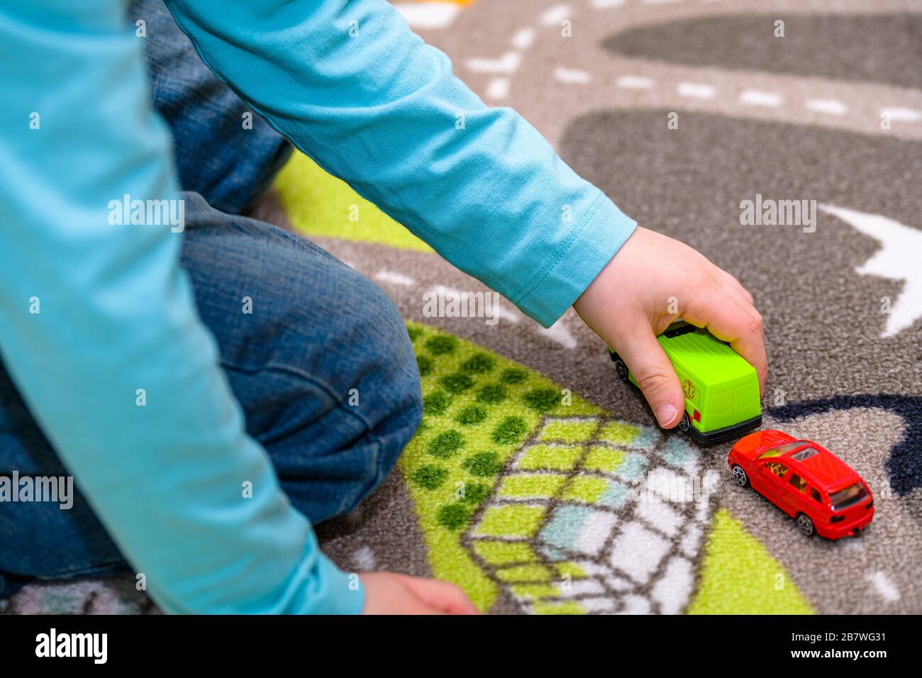 Ragazzo di cinque anni che gioca e allineano le auto giocattolo su un tappetino da gioco con le strade. Il ragazzo è vestito di jeans blu e tiene un giocattolo ambulanza. Foto Stock