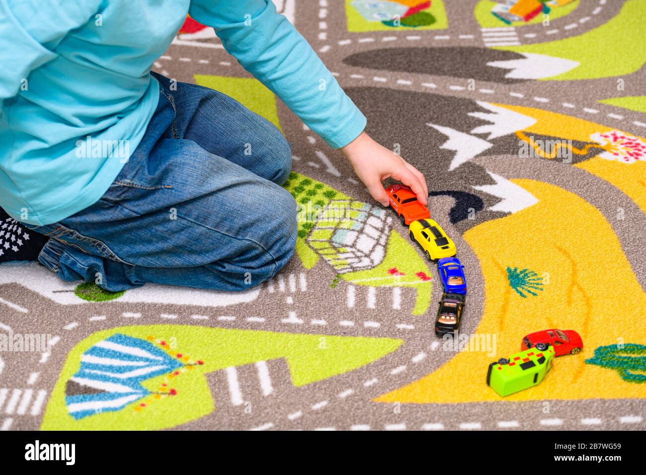 Ragazzo di cinque anni che gioca e allineano le auto giocattolo su un tappetino da gioco con le strade. Il ragazzo è vestito con jeans blu e tiene un camion rosso giocattolo pickup. Foto Stock