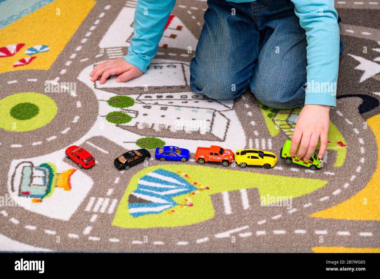 Ragazzo di cinque anni che gioca e allineano le auto giocattolo su un tappetino da gioco con le strade. Il ragazzo è vestito di jeans blu e tiene un giocattolo ambulanza. Foto Stock