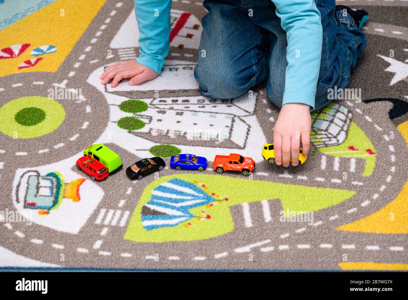 Ragazzo di cinque anni che gioca e allineano le auto giocattolo su un tappetino da gioco con le strade. Le auto hanno colori vivaci e il ragazzo è vestito di jeans blu. Foto Stock