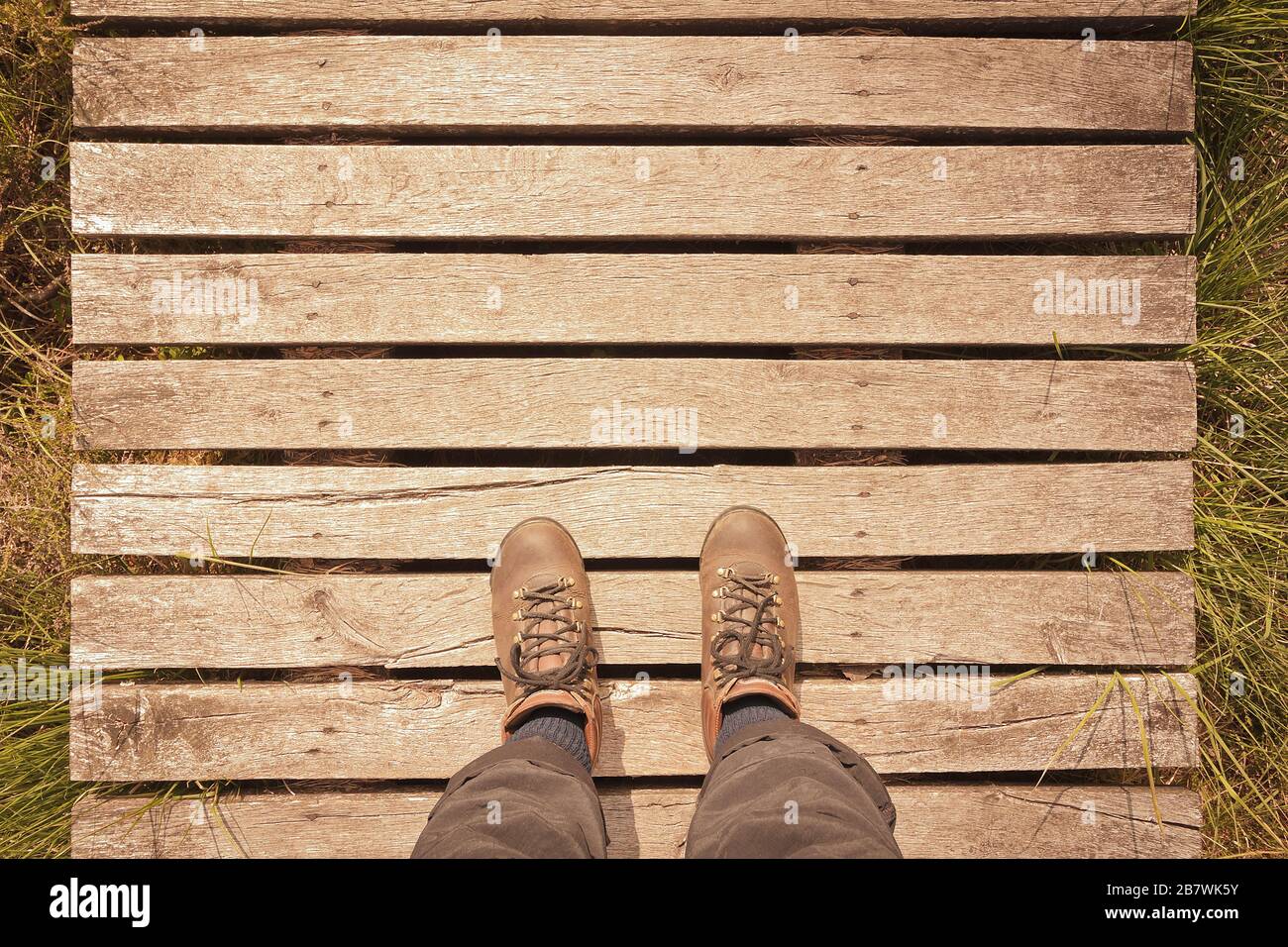 Stivali da trekking su una passerella in legno con spazio copia, concetto pov, effetto filtro vintage. Foto Stock