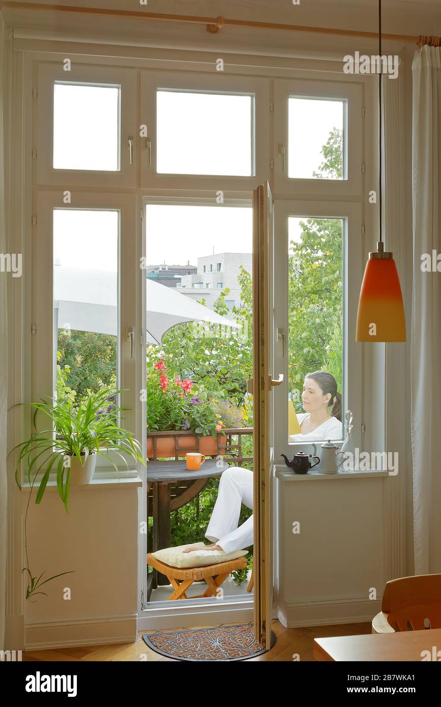 Donna di mezza età che legge un libro sul balcone di una vecchia casa cittadina in estate. Foto Stock