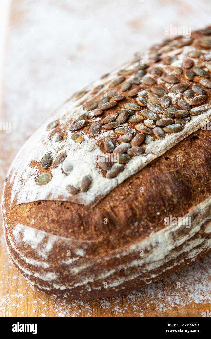 Immagine ravvicinata di una pagnotta di pane multigranato con semi di zucca su un tagliere infarinato Foto Stock