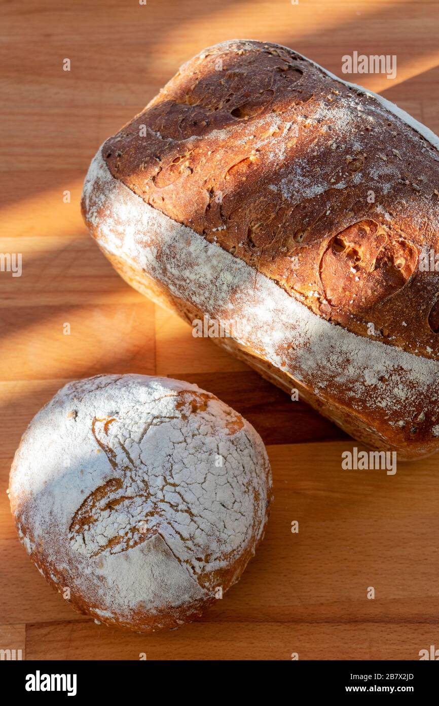 2 pagnotte di pane appena sfornato fatto in casa su un tagliere di legno Foto Stock