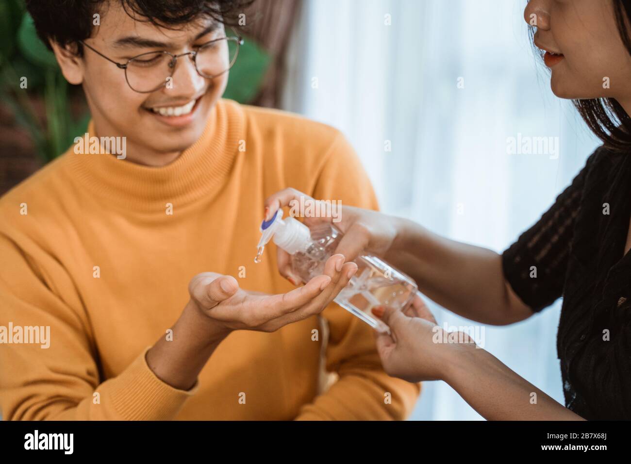 donna asiatica e uomo con igienizzatore a mano a casa Foto Stock