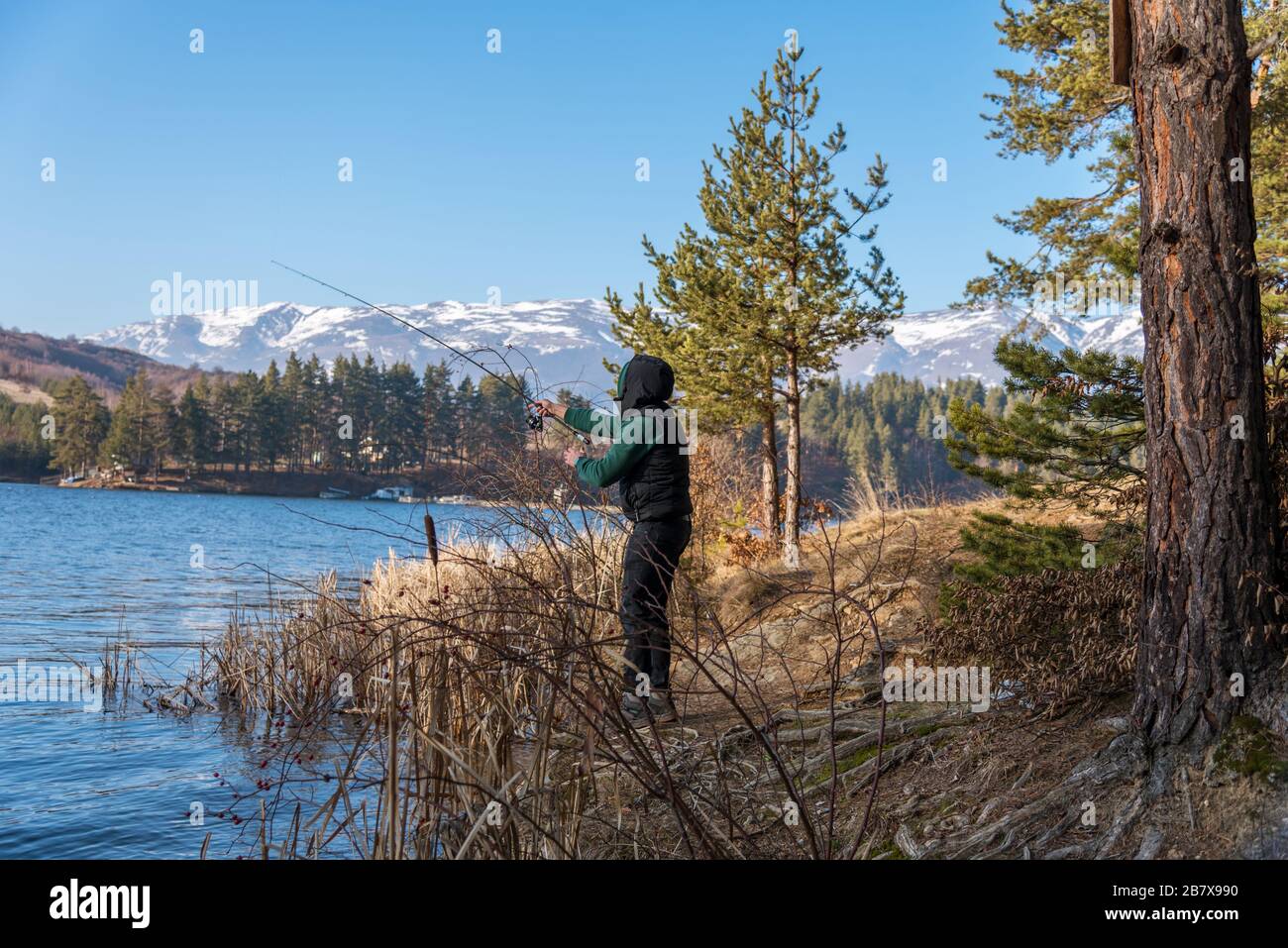 Un pescatore maschio sul lago è in piedi in acqua e la pesca per una canna da pesca. Concetto di vacanza hobby di pesca. Spazio di copia. Foto Stock