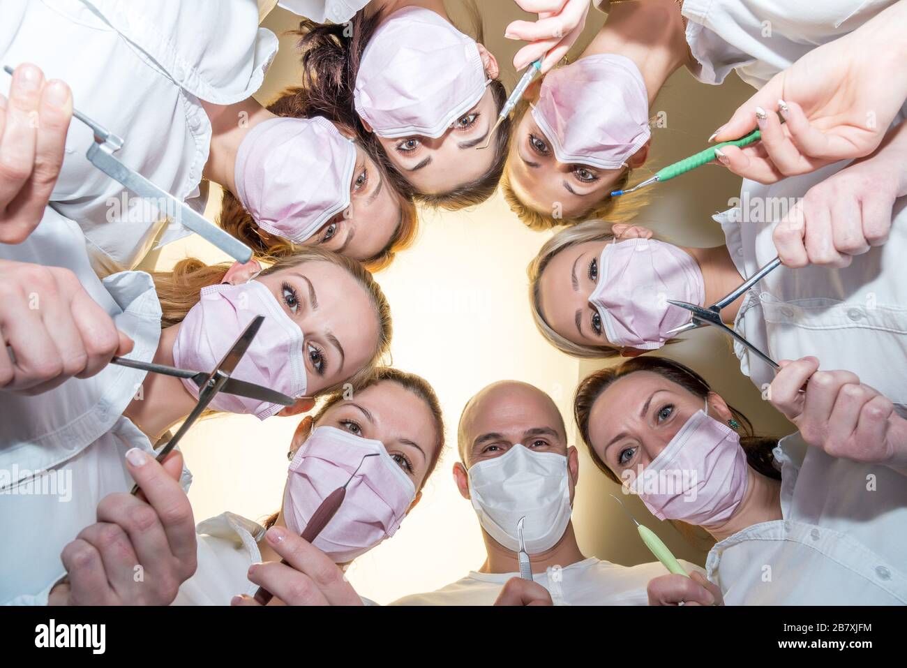 Un team di dentisti con strumenti e maschere che si piegano sul paziente Foto Stock