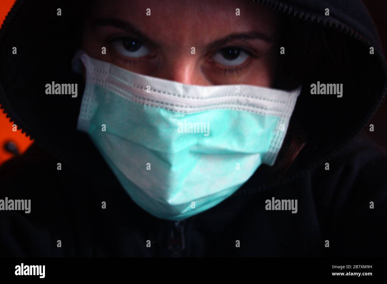 Un misterioso individuo con cappuccio irriconoscibile con felpa scura indossa una normale maschera chirurgica blu in italia Foto Stock