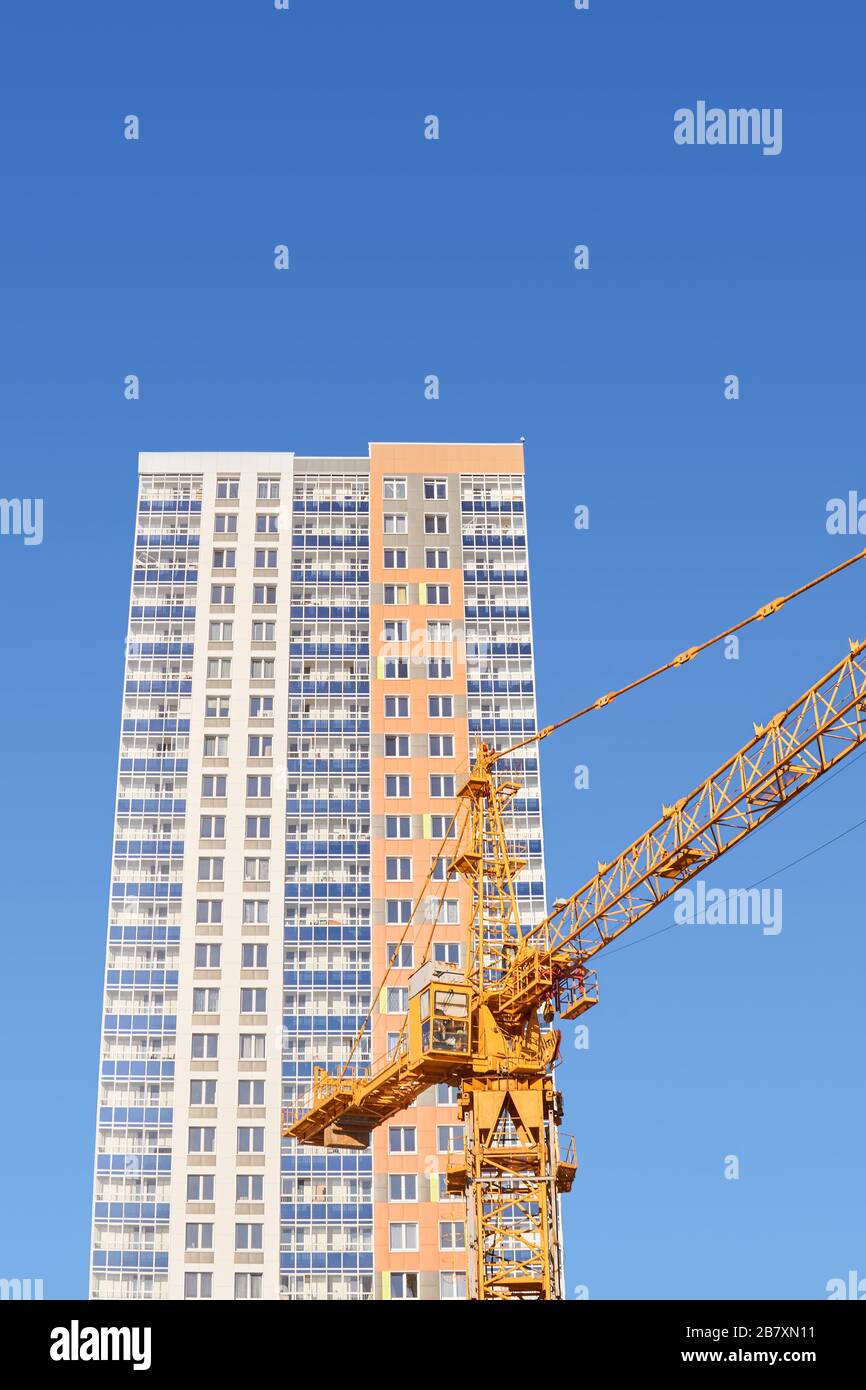 costruzione a più piani - cabina e braccio di una gru a torre e la parte superiore di un edificio residenziale multi-appartamento di nuova costruzione contro il blu Foto Stock