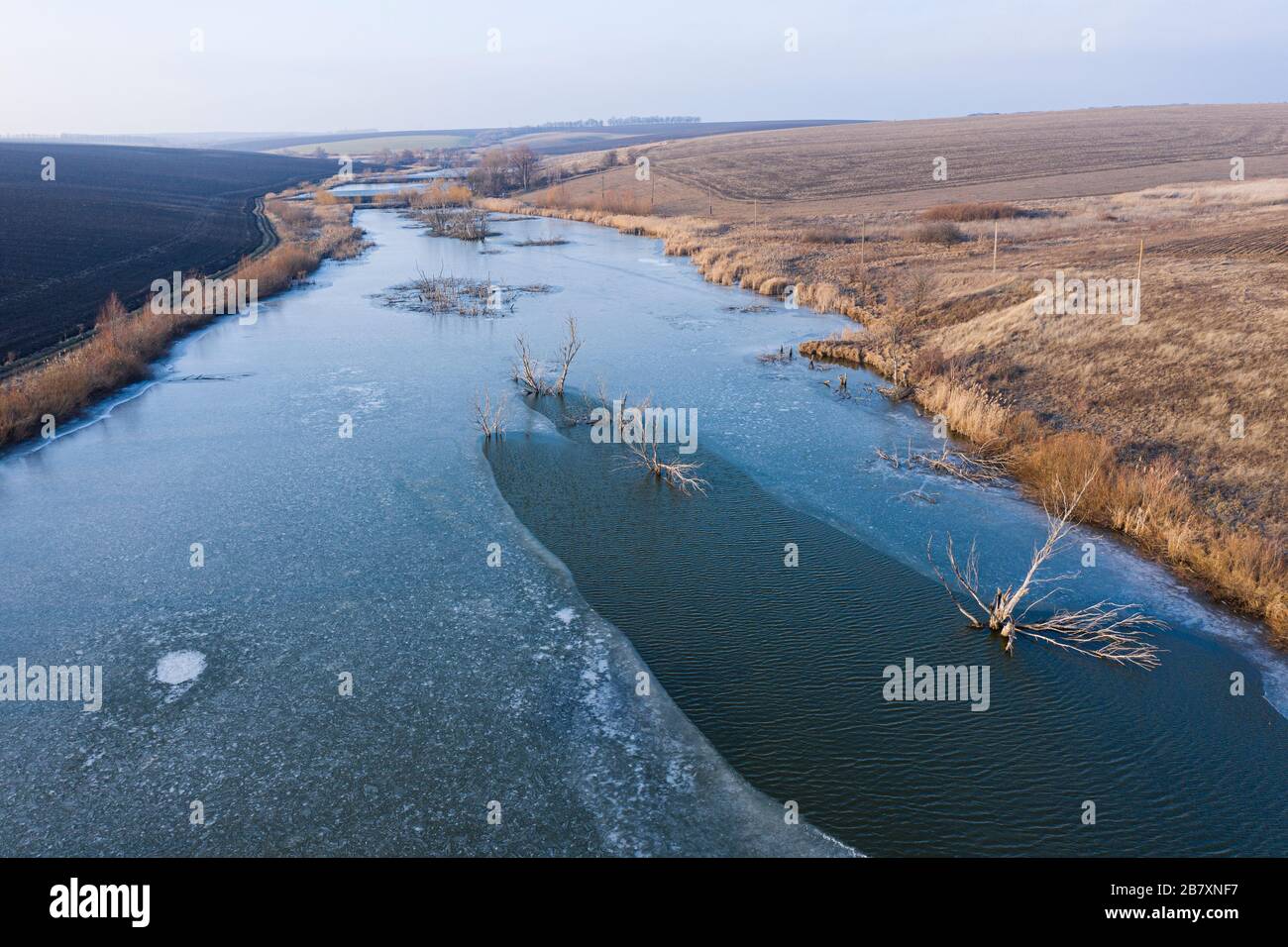 Volare un drone su un fiume. Alberi crescono in acqua di stagno. Ghiaccio e acqua allo stesso tempo. Basso vola sull'acqua nel mezzo del fiume. Un lungo riv Foto Stock