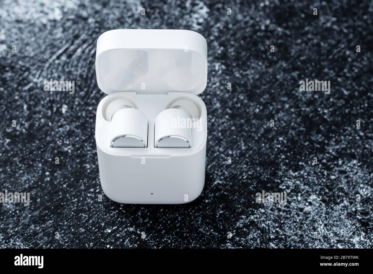 Auricolari Bluetooth bianchi con custodia di ricarica su sfondo scuro e sporco. Gadget per ascoltare musica. Dispositivo elettronico. Spazio vuoto per il testo Foto Stock