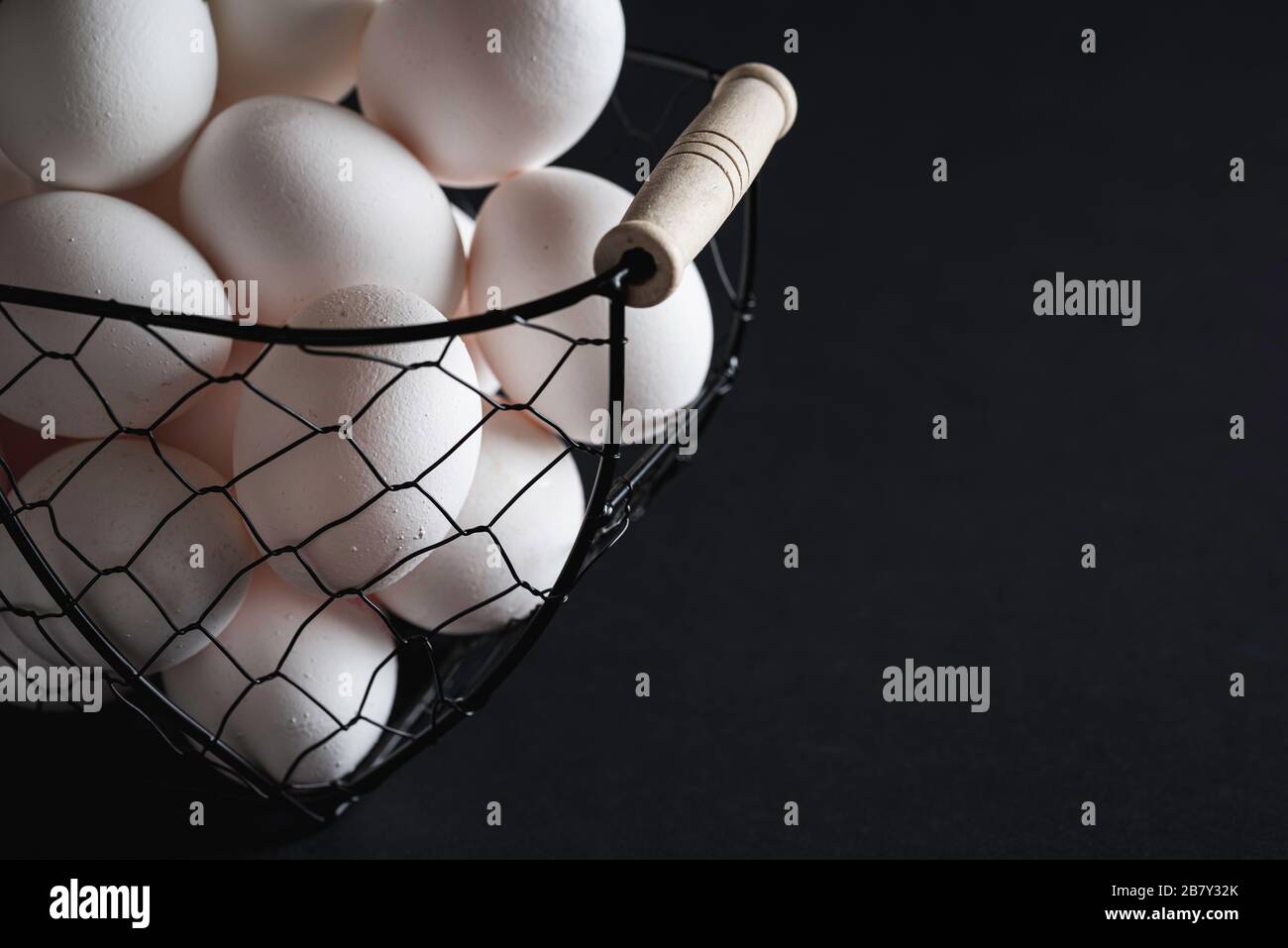 Uova bianche in un cesto di ferro su tavolo nero, in scarsa luce. Uova di pollo fresche, una ricca fonte di proteine. Foto Stock