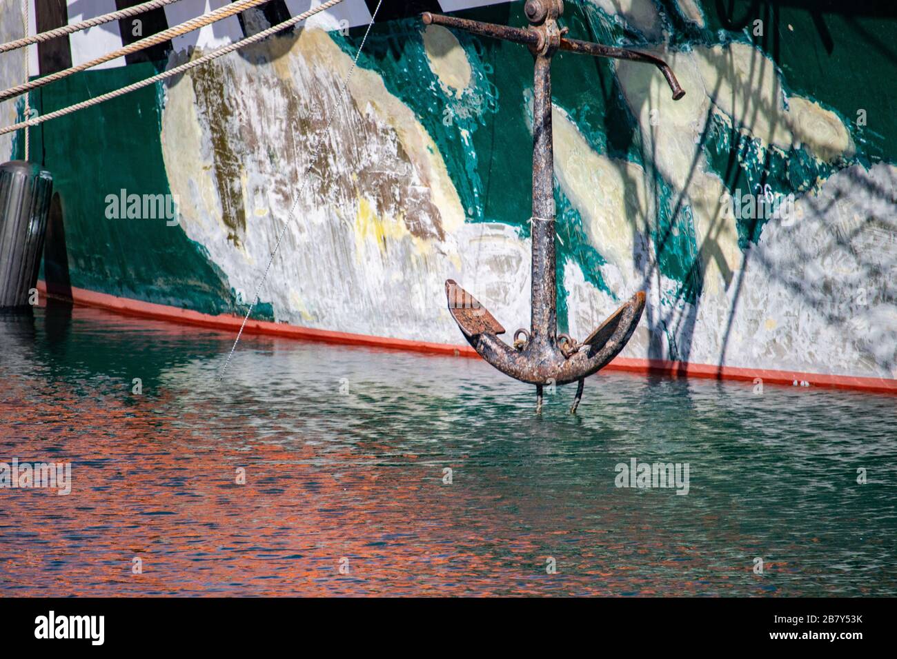 L'ancora di una barca grungy è visto appendere sopra l'acqua increspata prima dello scafo della barca. Foto Stock