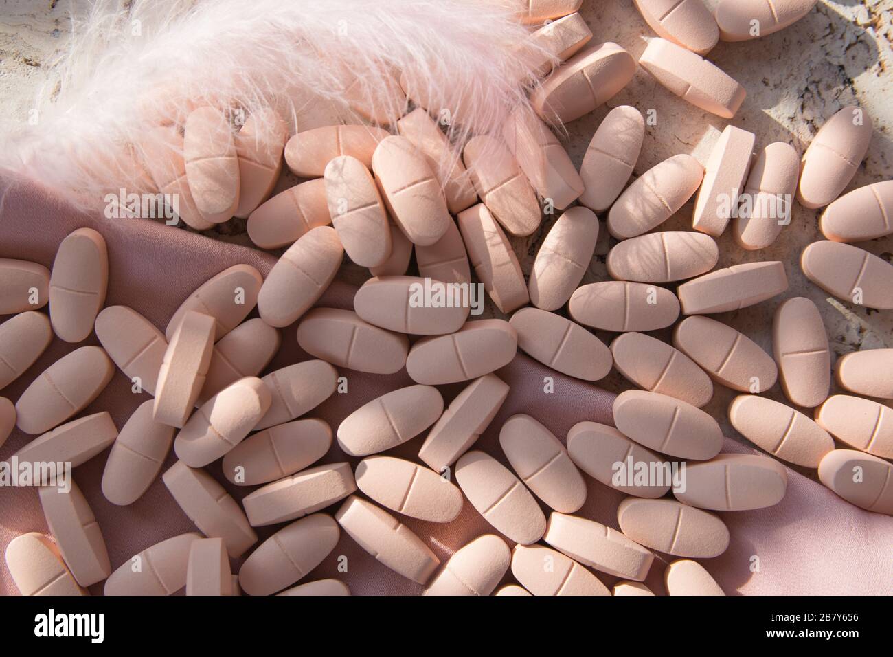 Pillole rosa o vitamine sullo sfondo naturale del legno con tessuto di seta rosa e piuma in estate. Vista dall'alto. Foto Stock