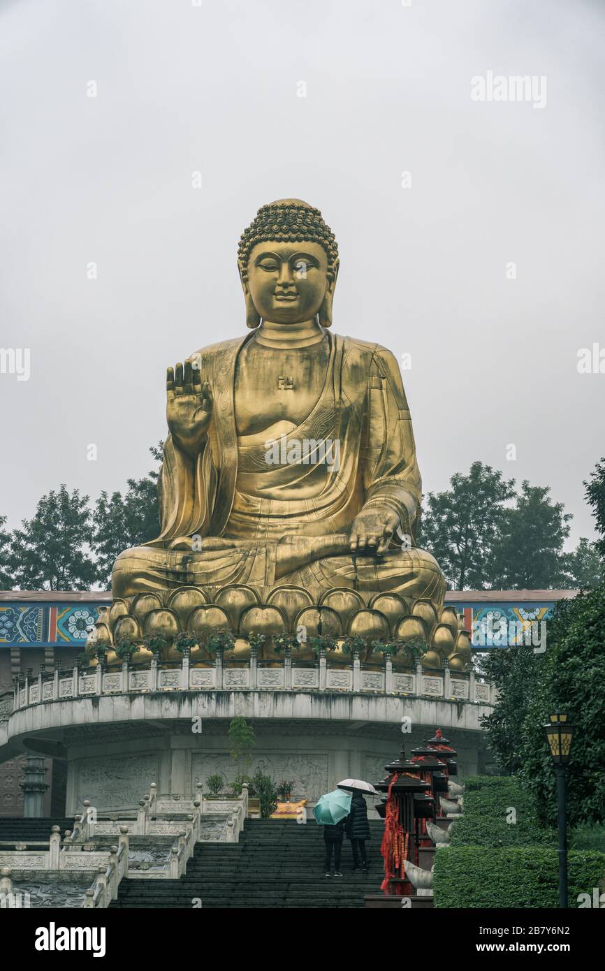 Le persone con umbrealla ammirano la statua dorata di Budda durante la pioggia nel Tempio di Hua Yan nella metropoli di Chongqing, Cina Foto Stock
