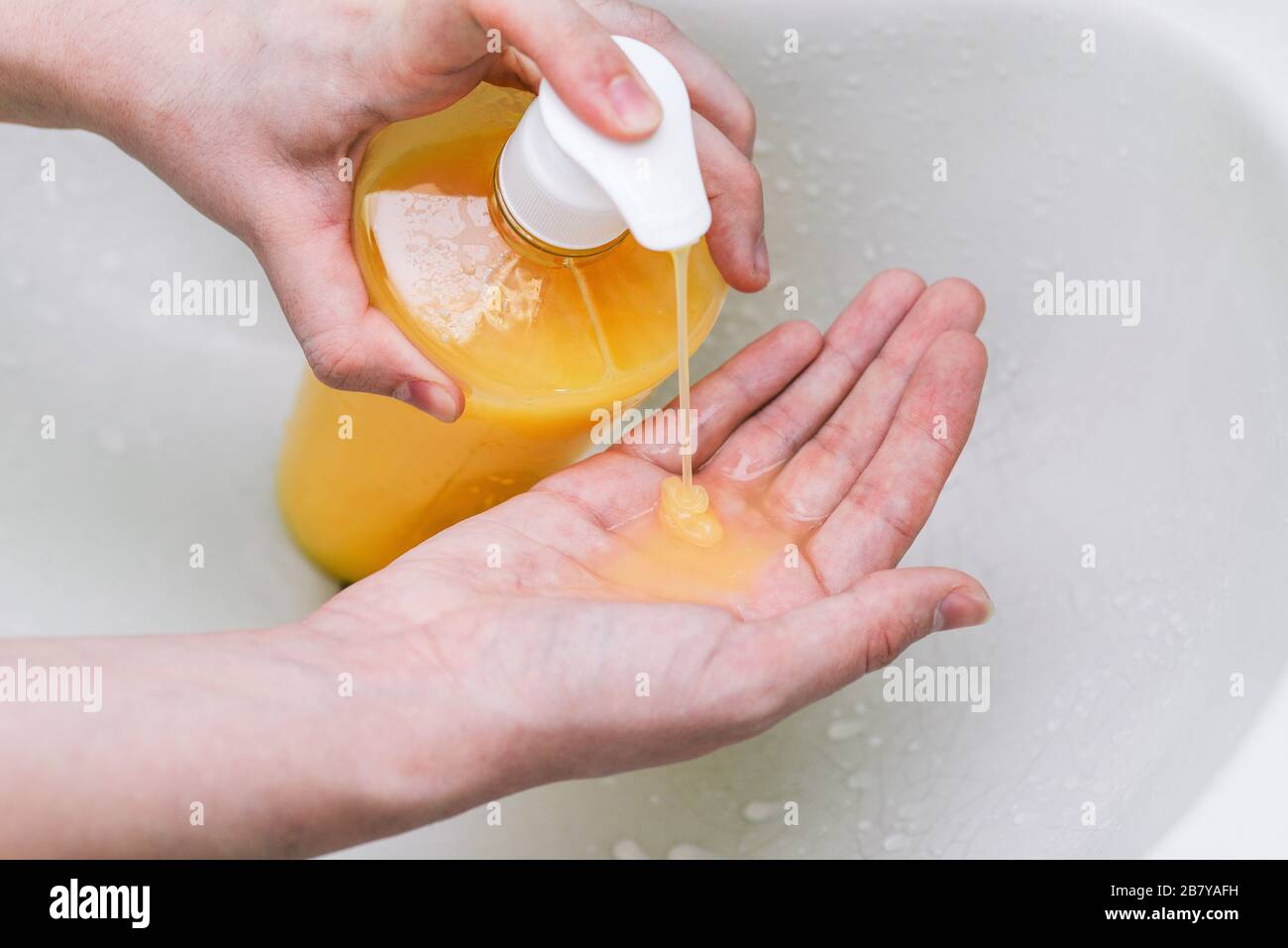 Donna strizza un disinfettante antibatterico sulle mani da una bottiglia di plastica. Liquido arancione denso per uccidere virus, germi e batteri Foto Stock