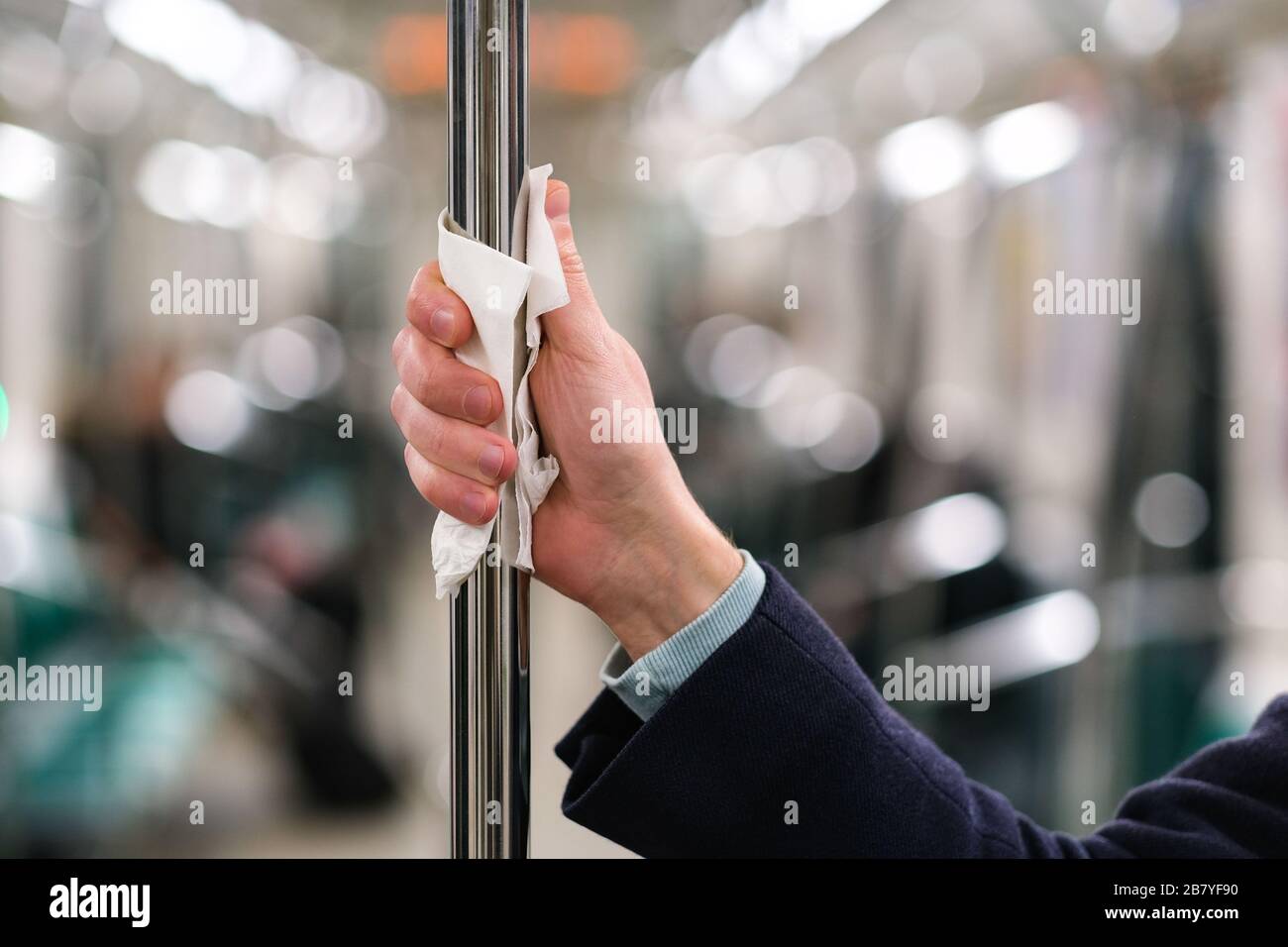 Primo piano della mano dell'uomo tiene un corrimano nel trasporto pubblico/metropolitana attraverso un tovagliolo, per proteggersi dal contatto con virus, germi durante un coron Foto Stock