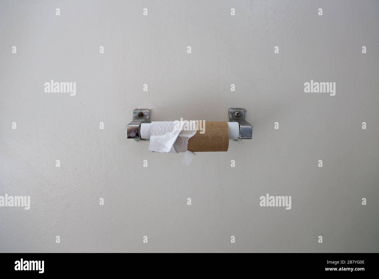 I residui strappati di un rotolo di carta igienica sono mostrati su un dispenser montato sulla parete bianca di un bagno. Foto Stock