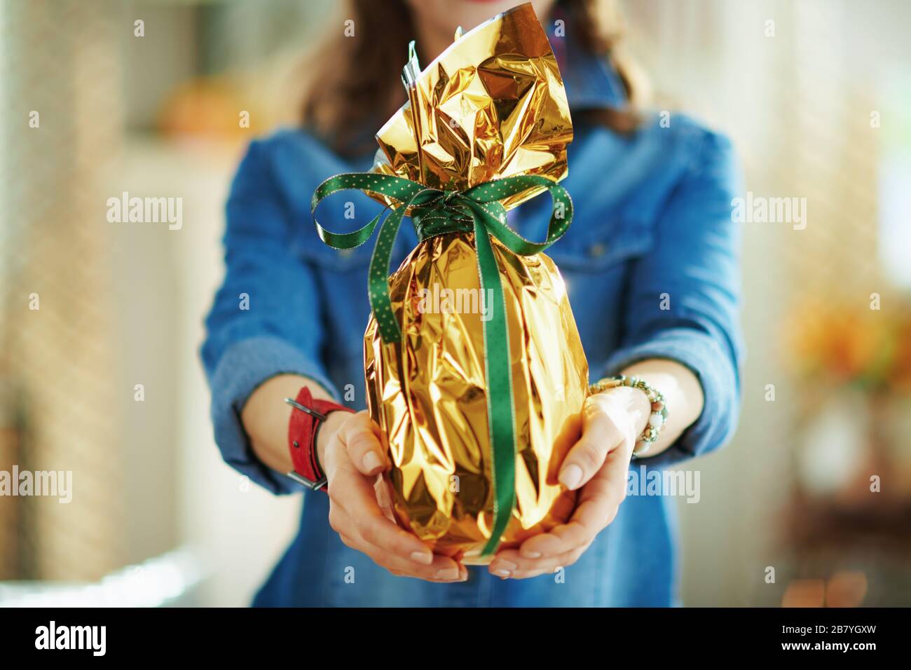 Primo piano su donna nel soggiorno in primavera giorno di sole dando avvolto in oro foglio grande uovo di pasqua. Foto Stock