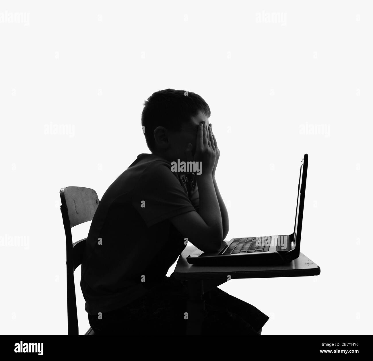 Uno studente bambino è seduto a una scrivania della scuola e sembra sconvolto e triste con un computer portatile per un concetto di Internet bully. Foto Stock