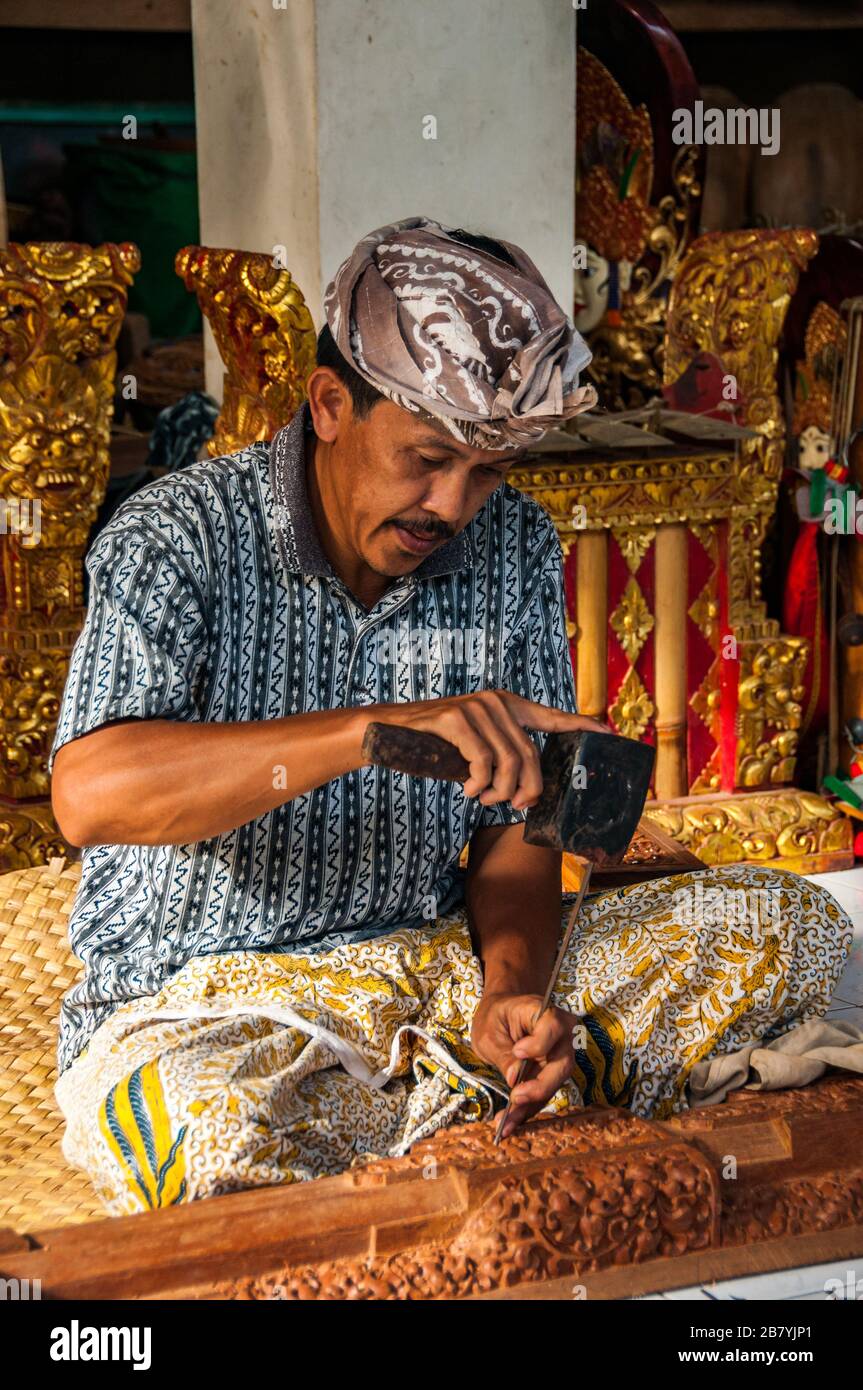 Un artigiano Balinese in un duro lavoro a scolpire una statua di un blocco di legno utilizzando un martello e scalpello. Foto Stock